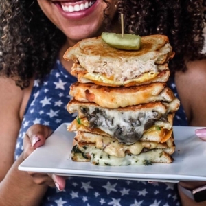 smiling-woman-holding-stack-of-grilled-cheese-sandwiches